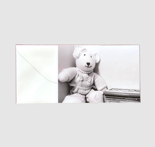 A black and white photo of a teddy bear beside a stack of children's books on the front of a greeting card.