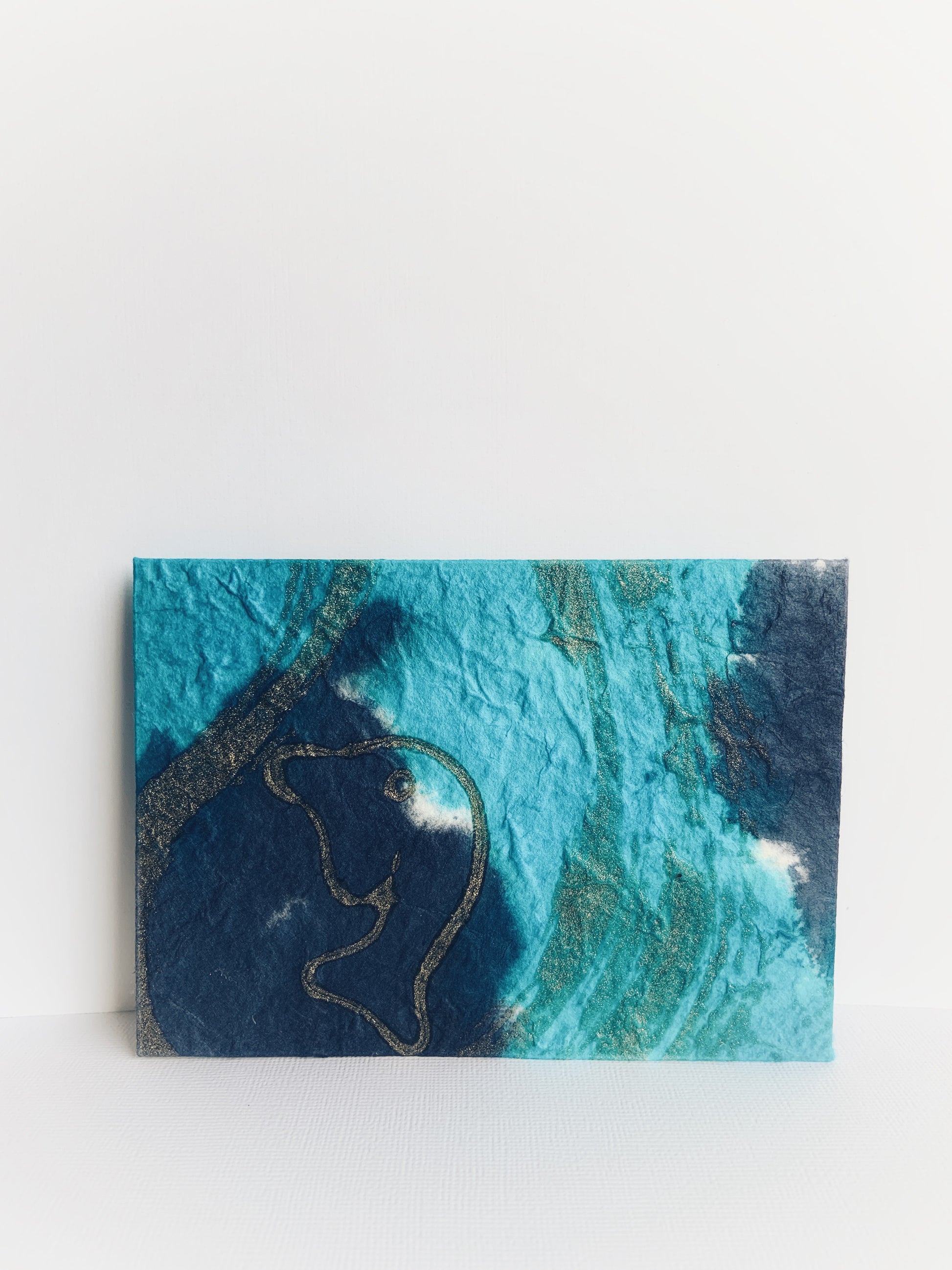 Front of a handmade light and dark blue envelope made from handmade paper from Thailand with a gold 'dolphin'.