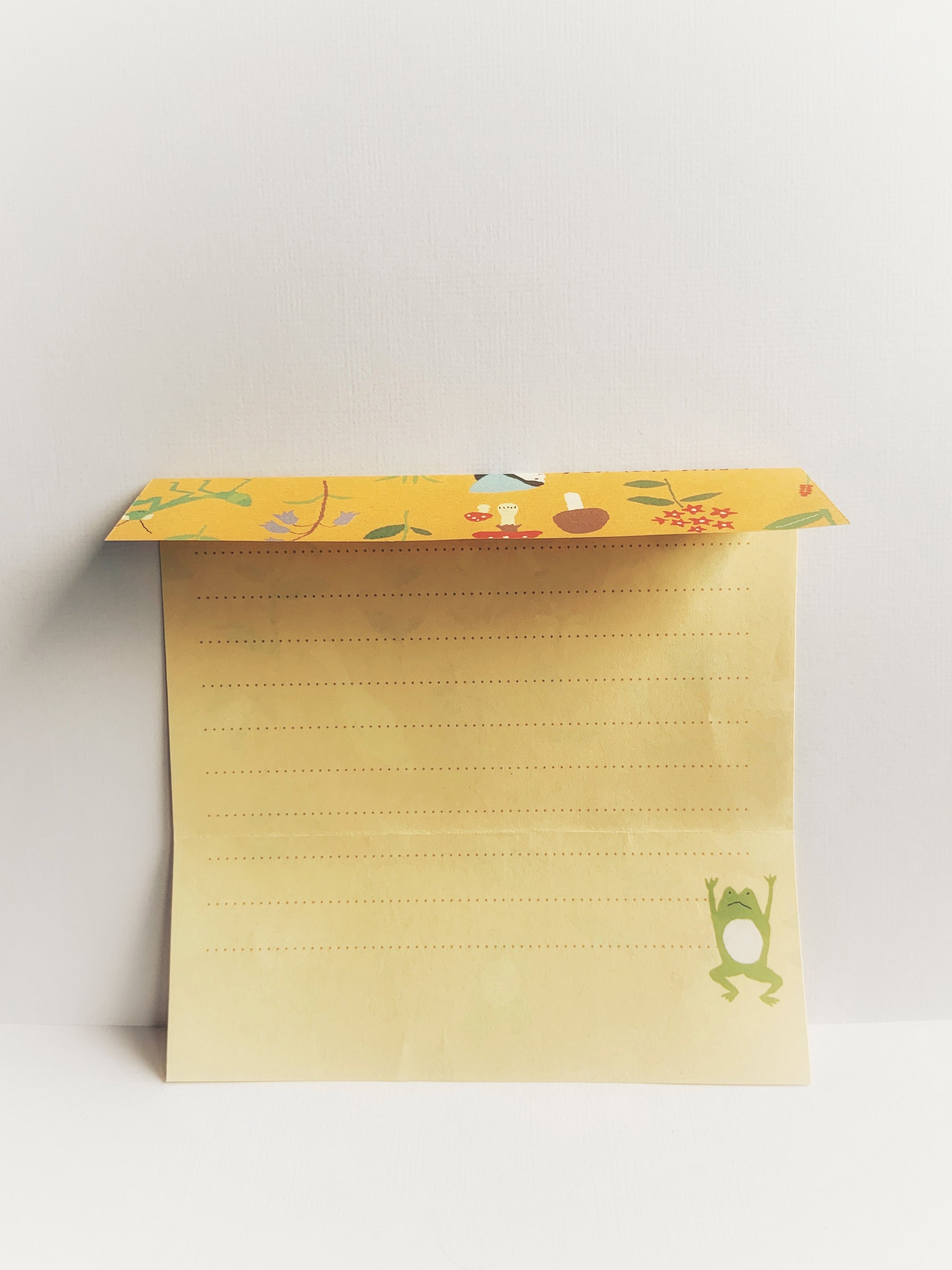 Yellow lined notepaper with a little green frog with a white belly jumping in the air