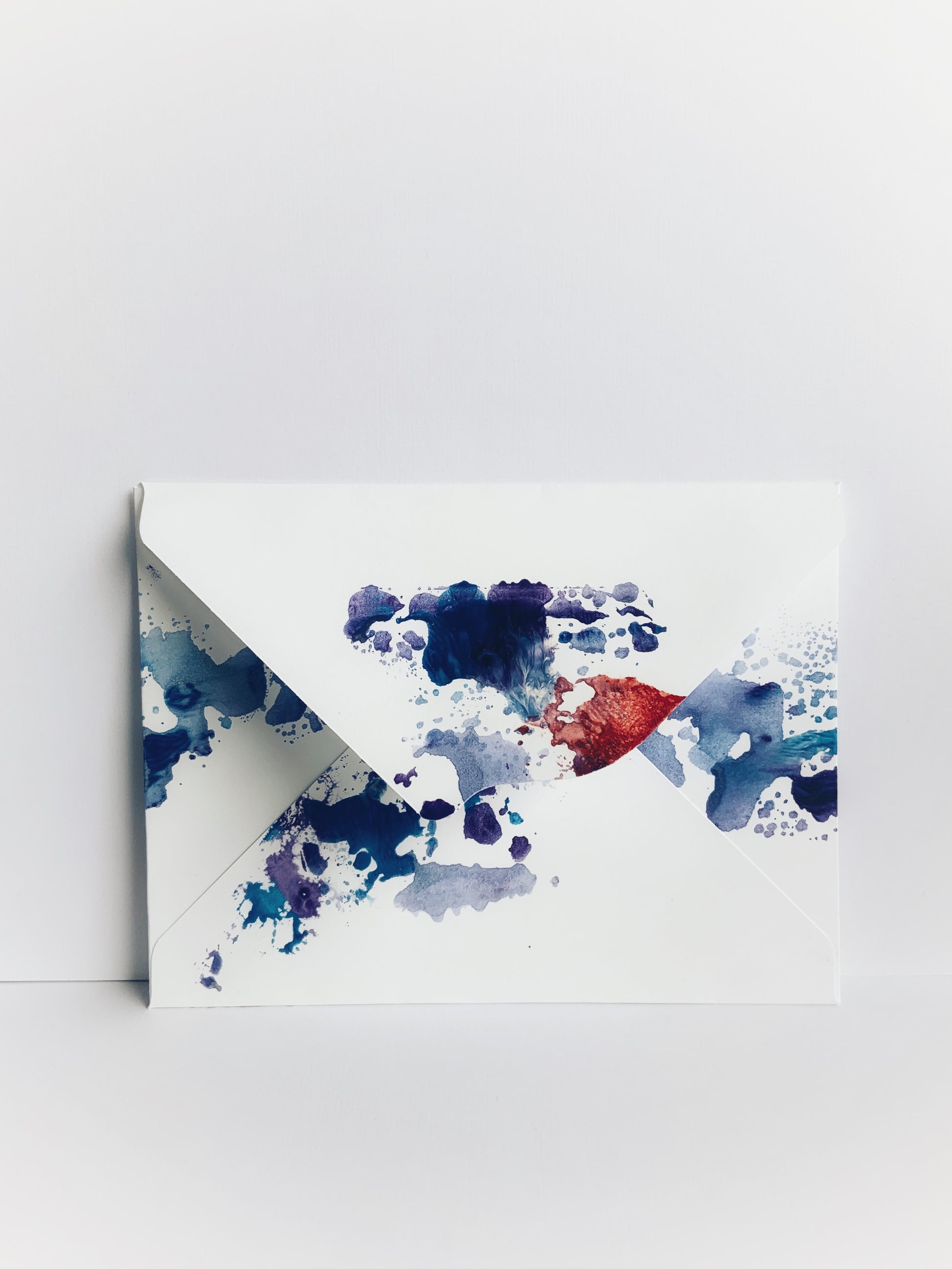 The back of a handmade envelope painted in blue and red watercolor with a scalloped flap