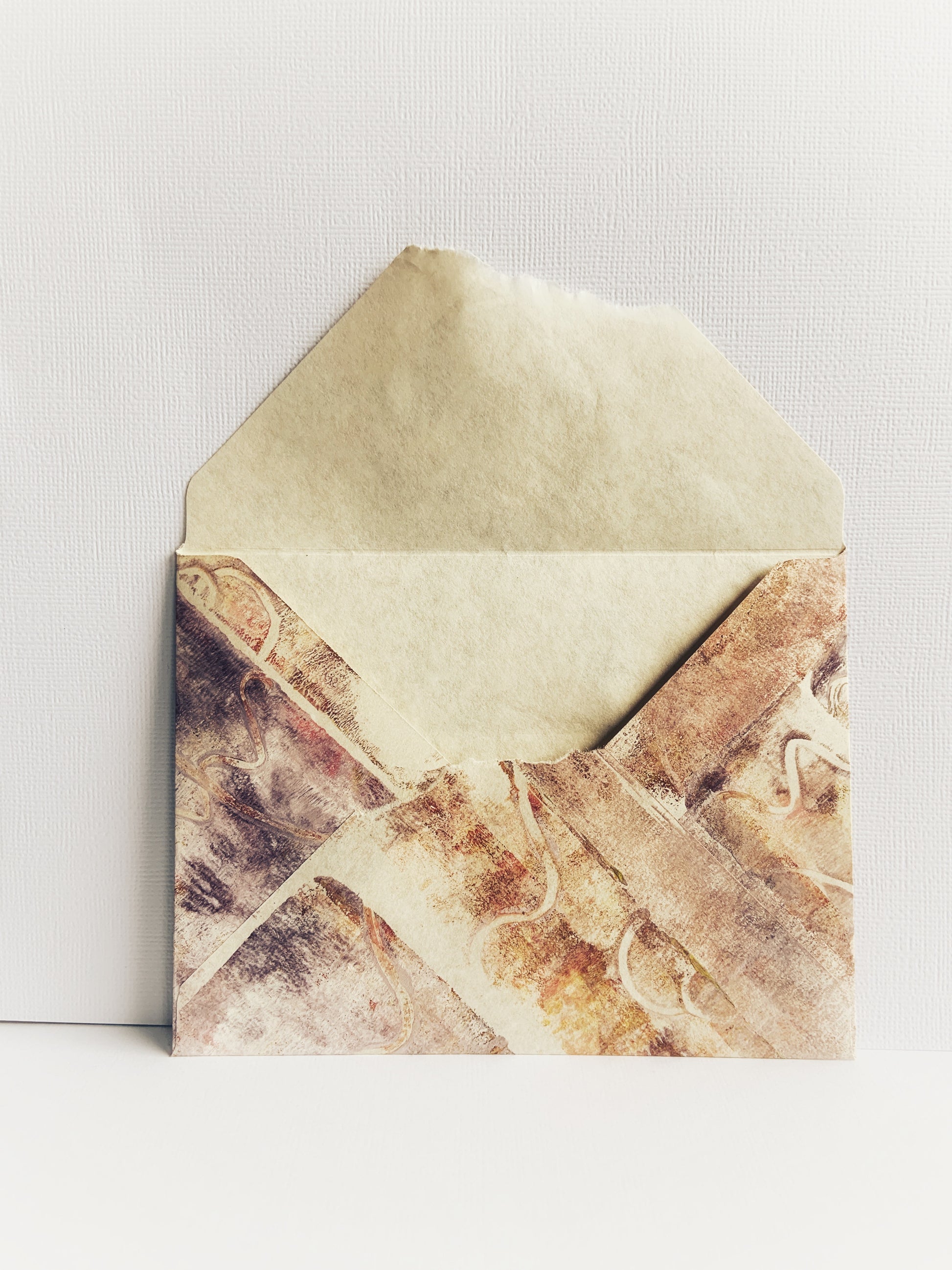 Back of a handmade envelope painted in muted brown and purple colors on natural-colored parchment paper with torn edge and flap