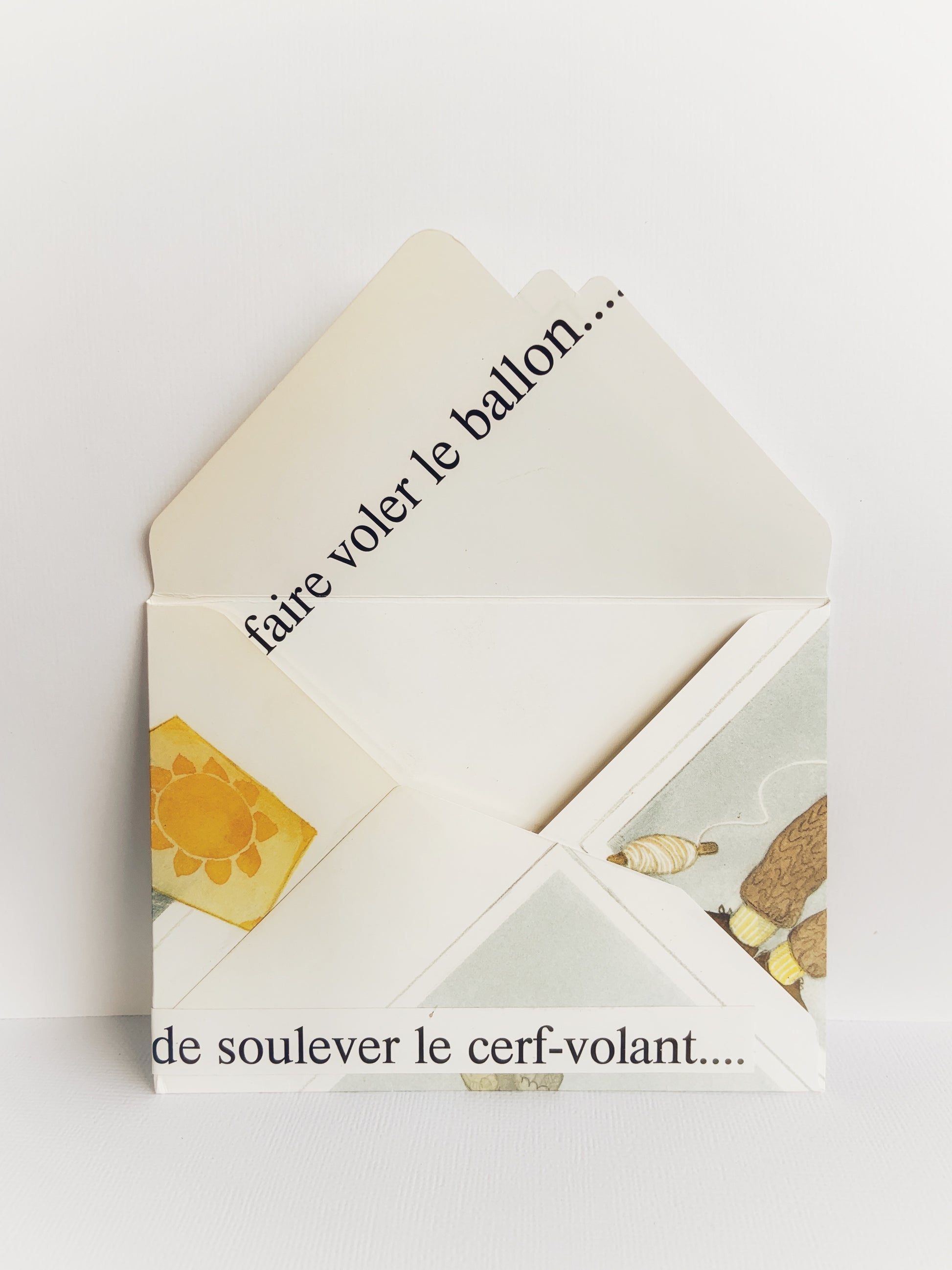 The back of a handmade envelope with the flap open that shows 'faire voler le ballon' across it and 'de soulever le cerf-volant' on the bottom.