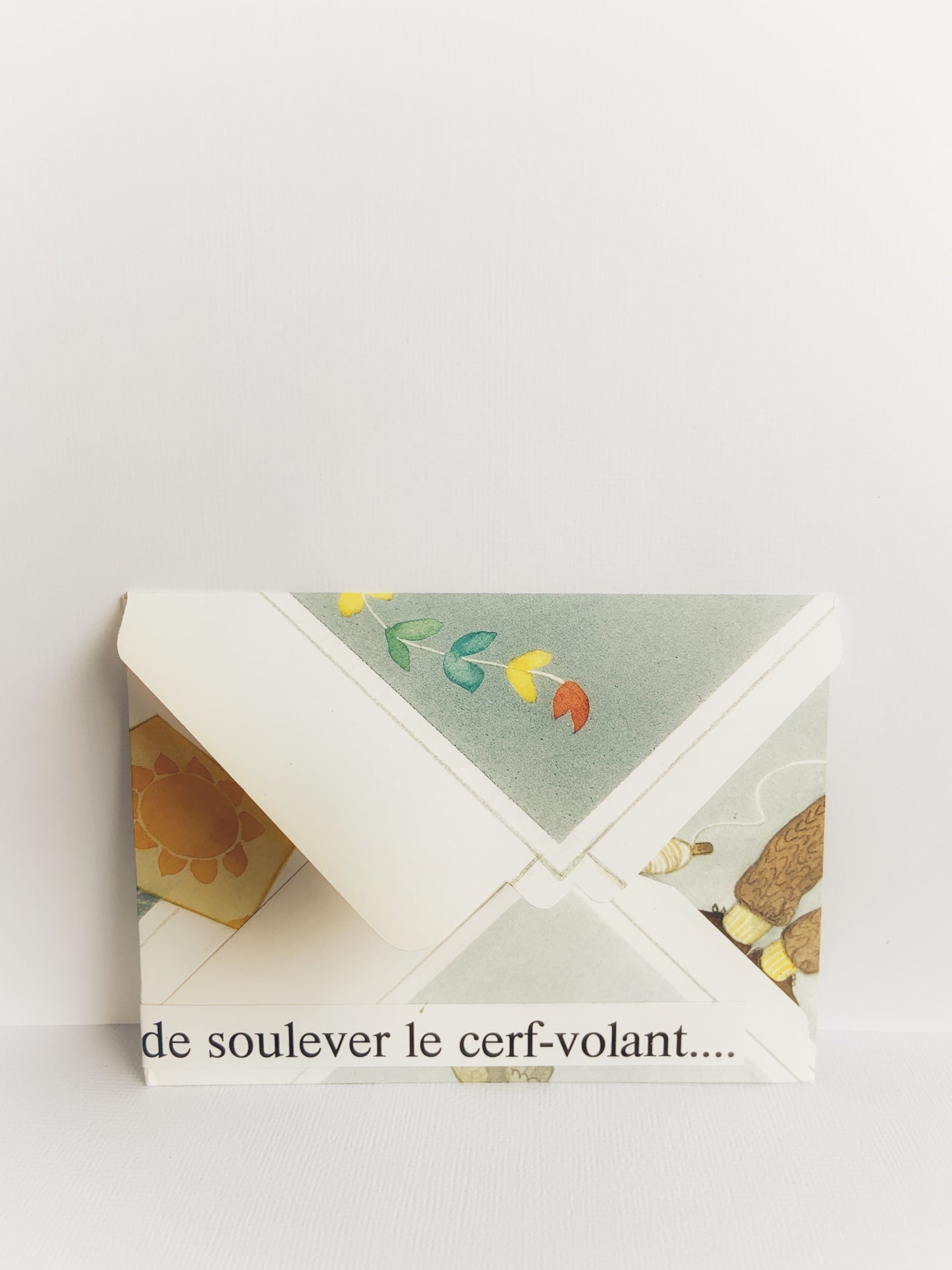 The back of a handmade colorful envelope showing the tail of a kite and 'de soulever le cerf-volant' at the bottom. 