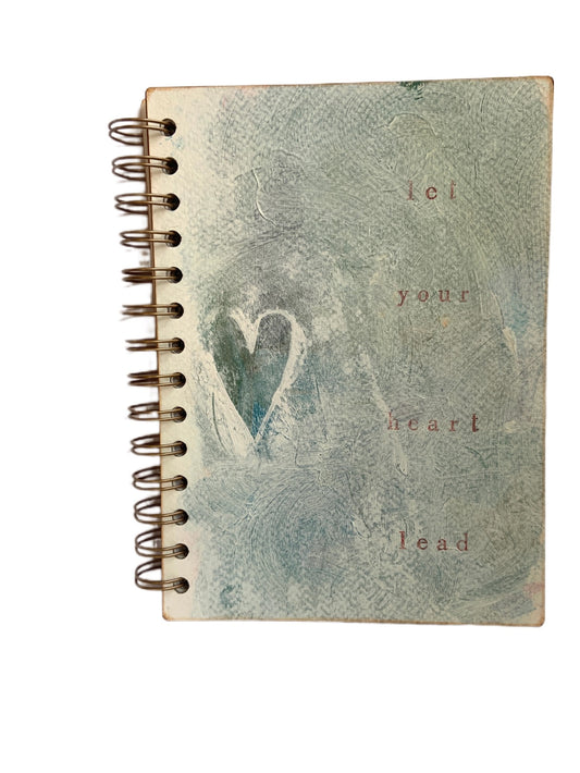 Front of medium handmade journal with a heart in muted blue and white tones with 'Let your heart lead' in muted red lettering.