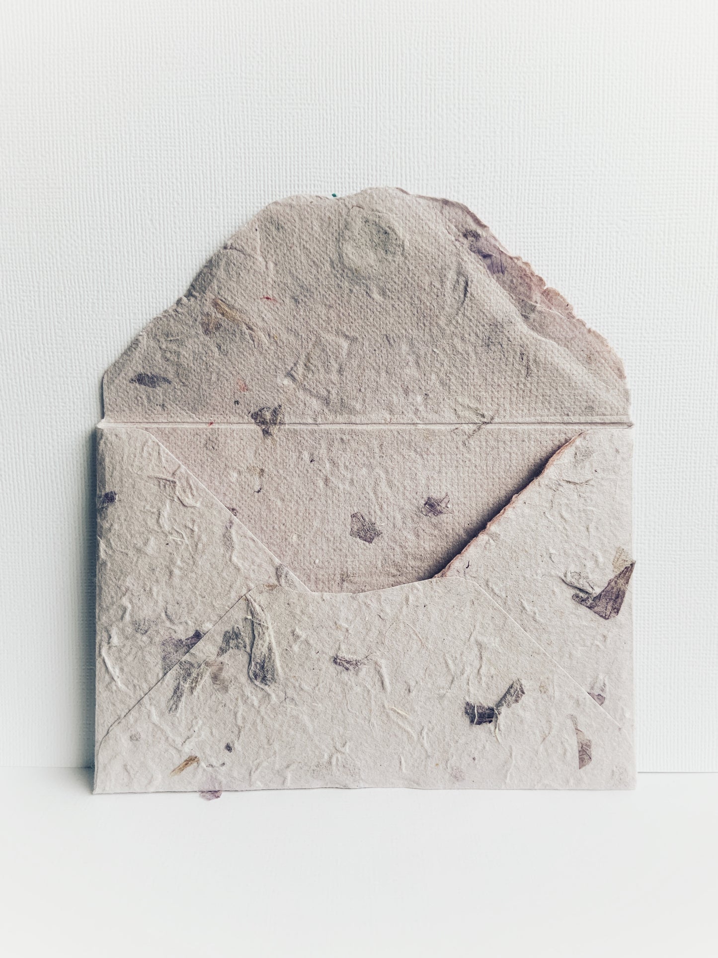 Back of a handmade envelope made from mauve handmade paper from Thailand showing detail on the inside and flap. Small pieces of dried flowers add to the paper's texture.