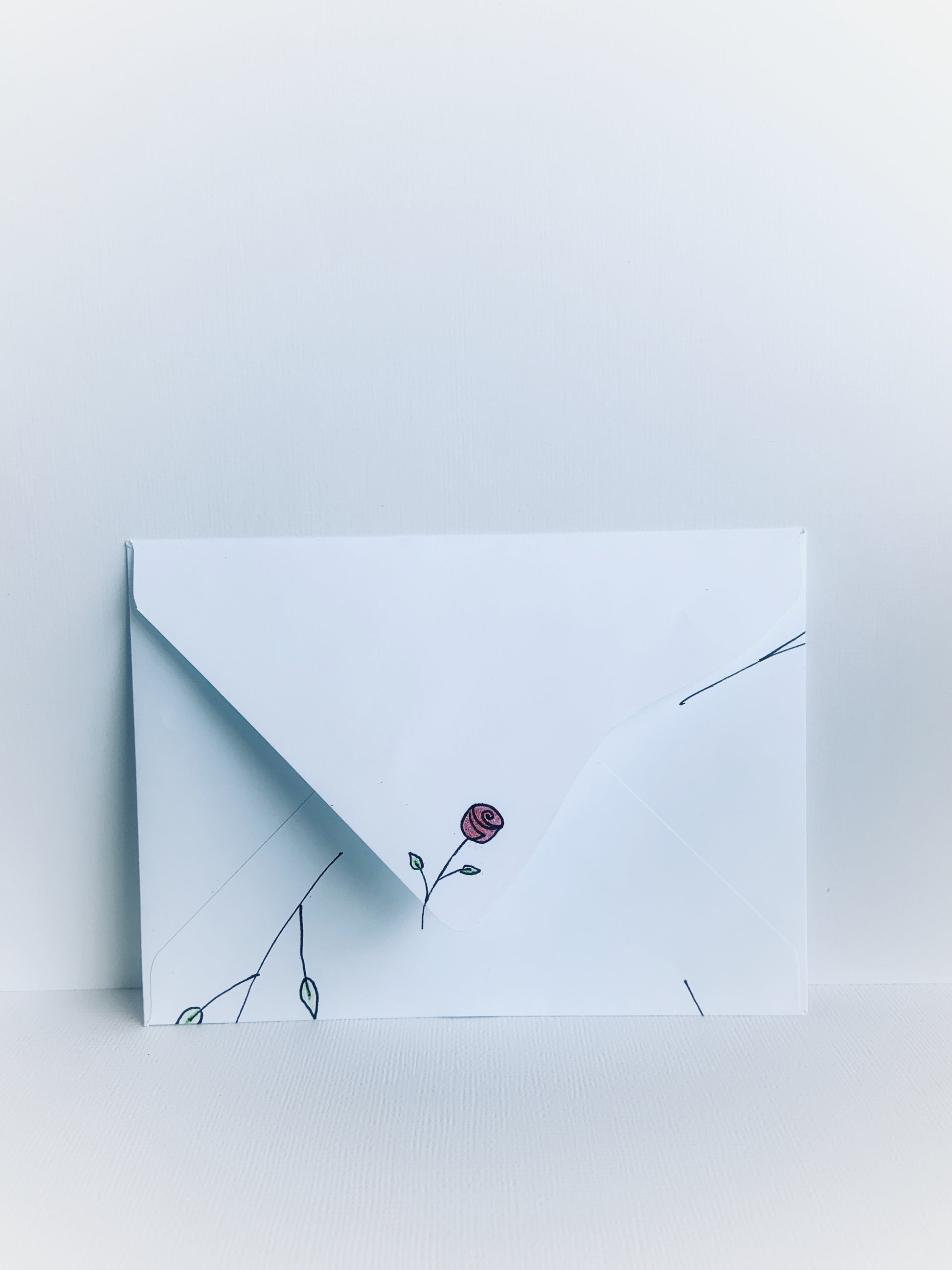 The back of a white handmade envelope with a tiny rosebud with stem and leaves on the point of the detailed  flap.