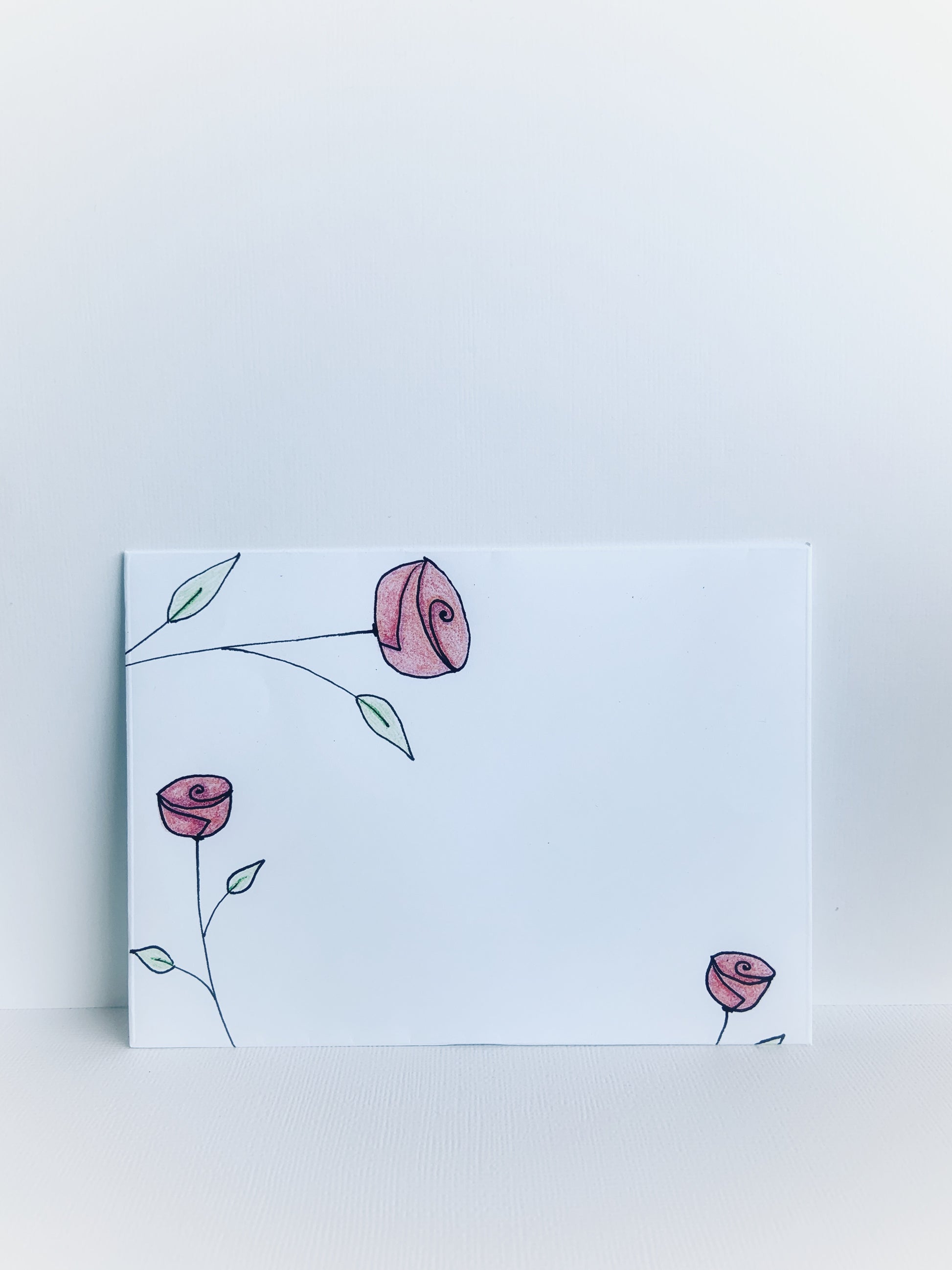 The front of a white handmade envelope with hand drawn pink rosebuds with stems and dainty leaves.