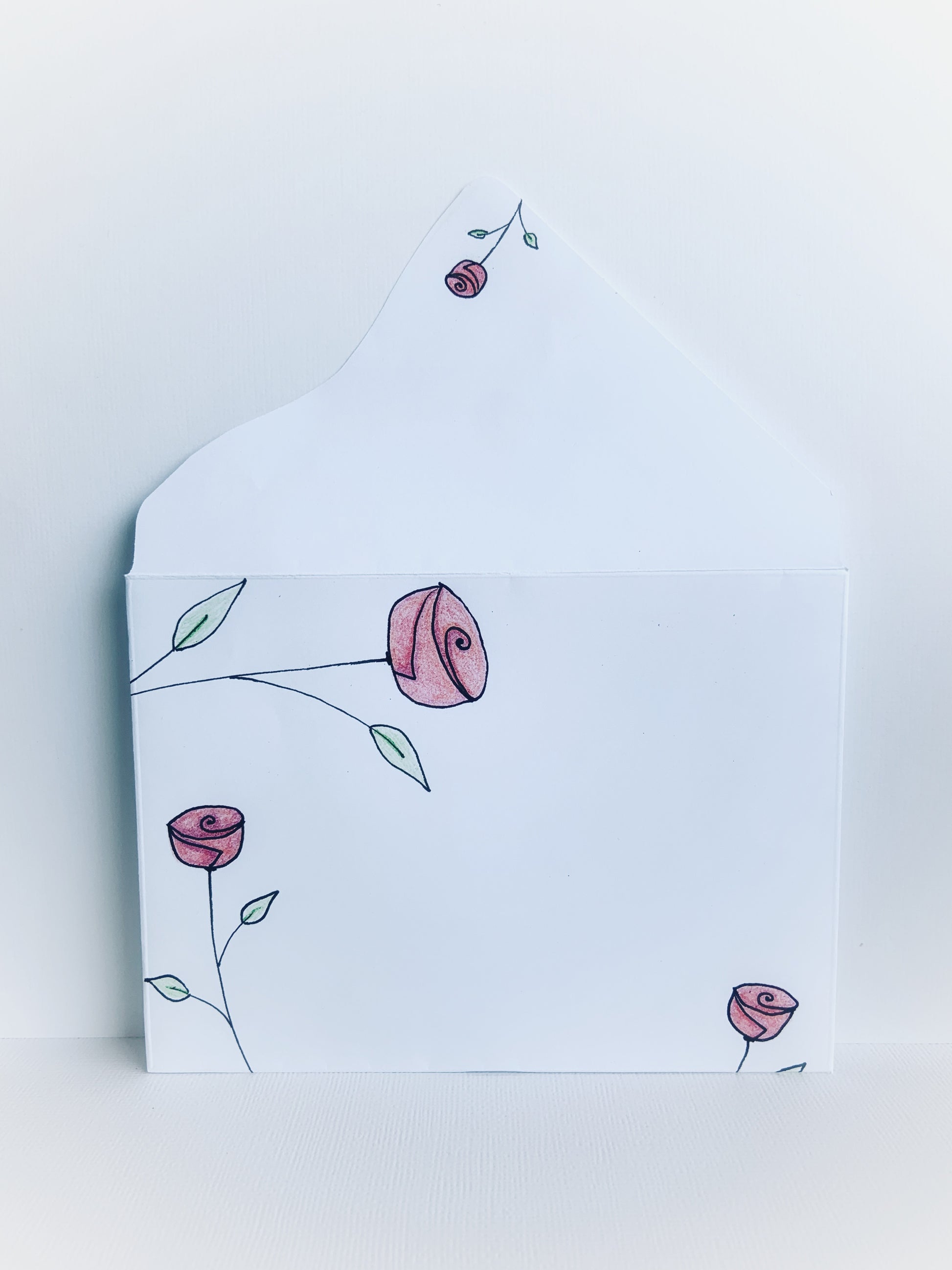 The front of a white handmade envelope with dainty hand drawn pink rosebuds with stems and little leaves and showing the detail on the back flap.