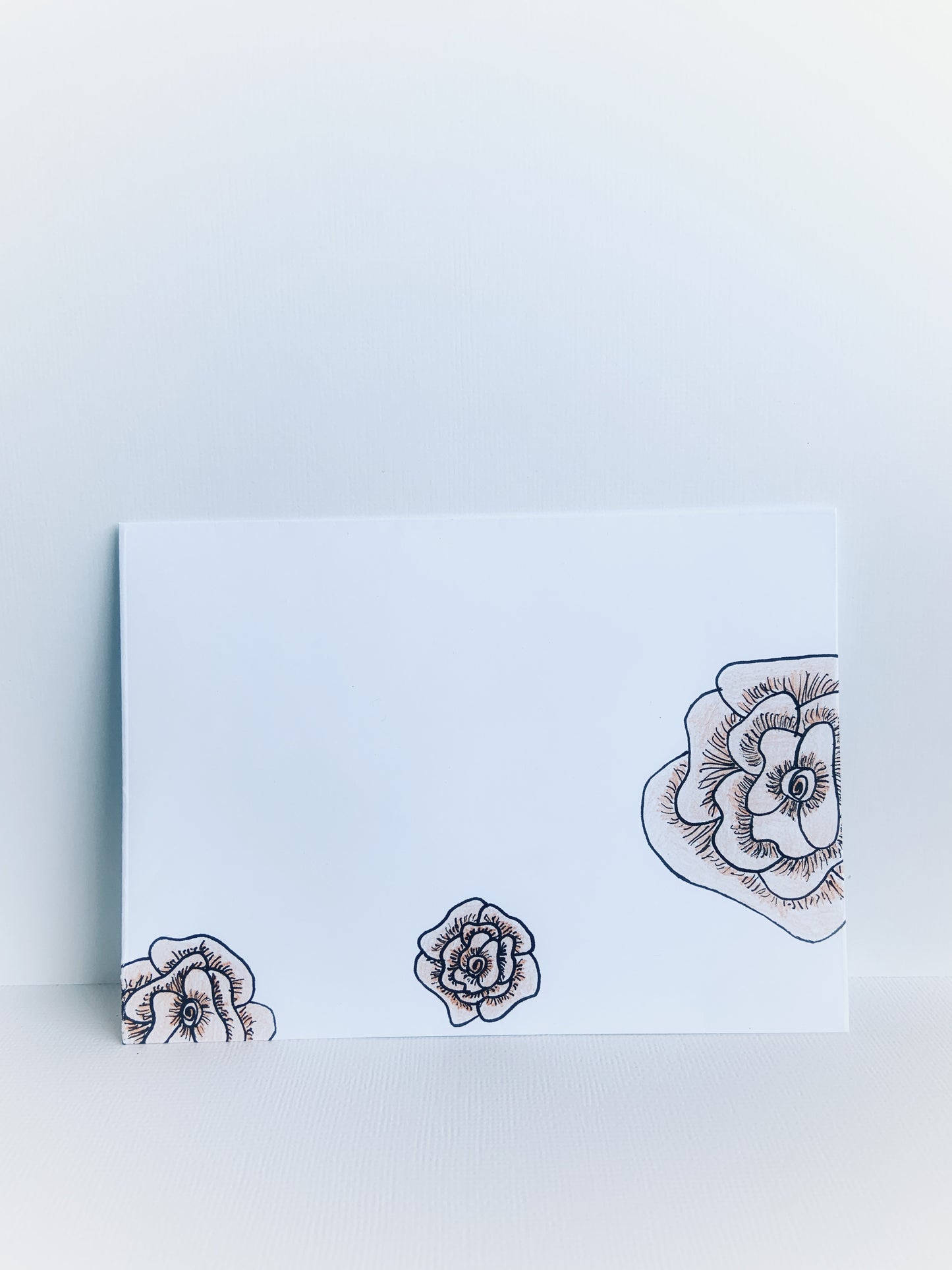 The front of a white handmade envelope with 3 black line drawn flowers colored with soft orange.
