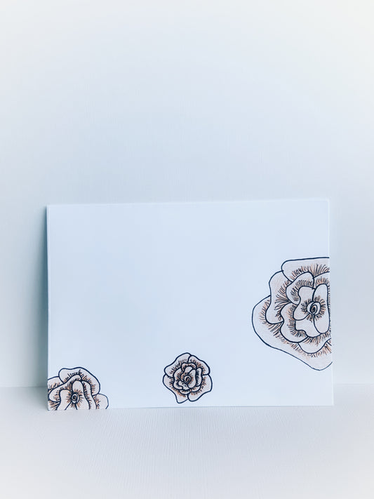 The front of a white handmade envelope with 3 black line drawn flowers colored with soft orange.