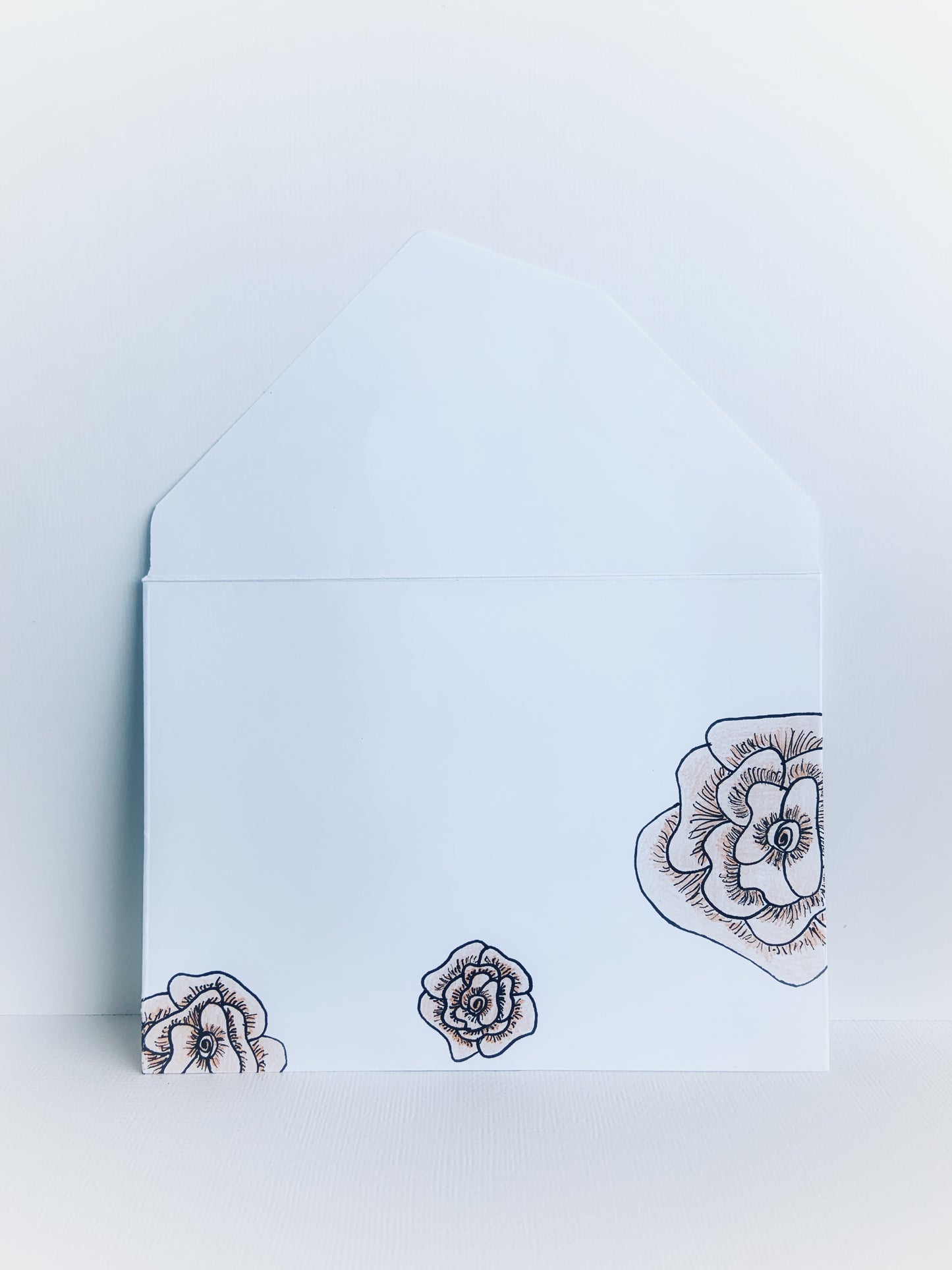 The front of a white handmade envelope with black line drawn flowers colored with soft orange showing detail on the flap.