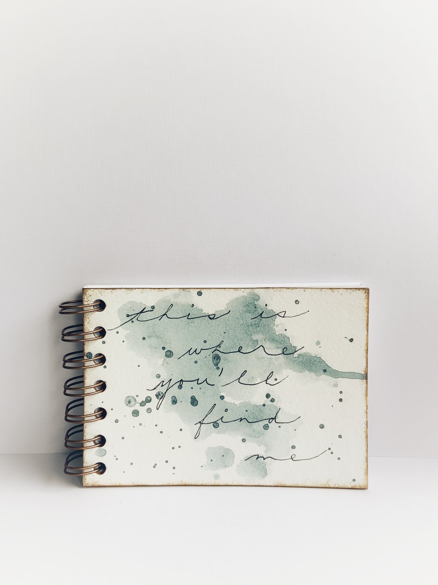 Small coil-bound handmade journal with 'this is where you'll find me' written on a paint-spattered cover