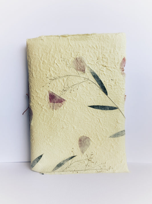 Front cover of handmade journal made from handmade paper from Thailand, yellow with dried flowers woven throughout.