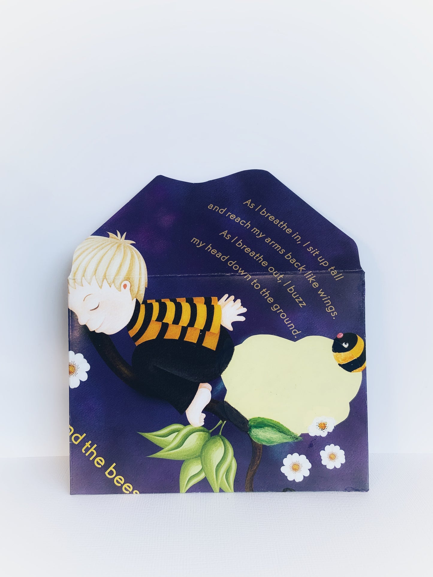 Front of an open handmade envelope showing a boy in child's pose and a bee and flowers and a paragraph about breathing in and out and moving the body.