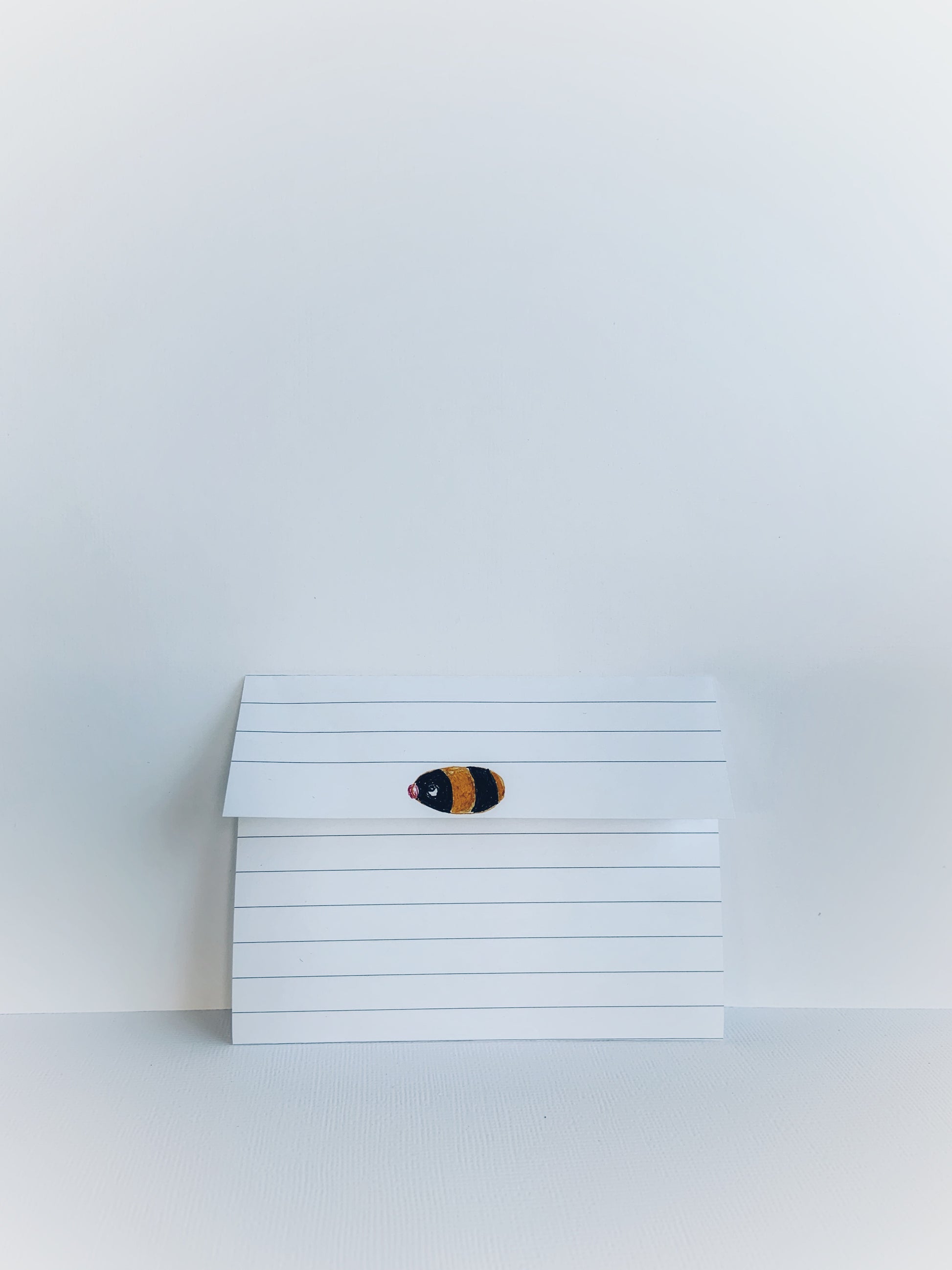 Folded lined notepaper with a little bee painted on the front.